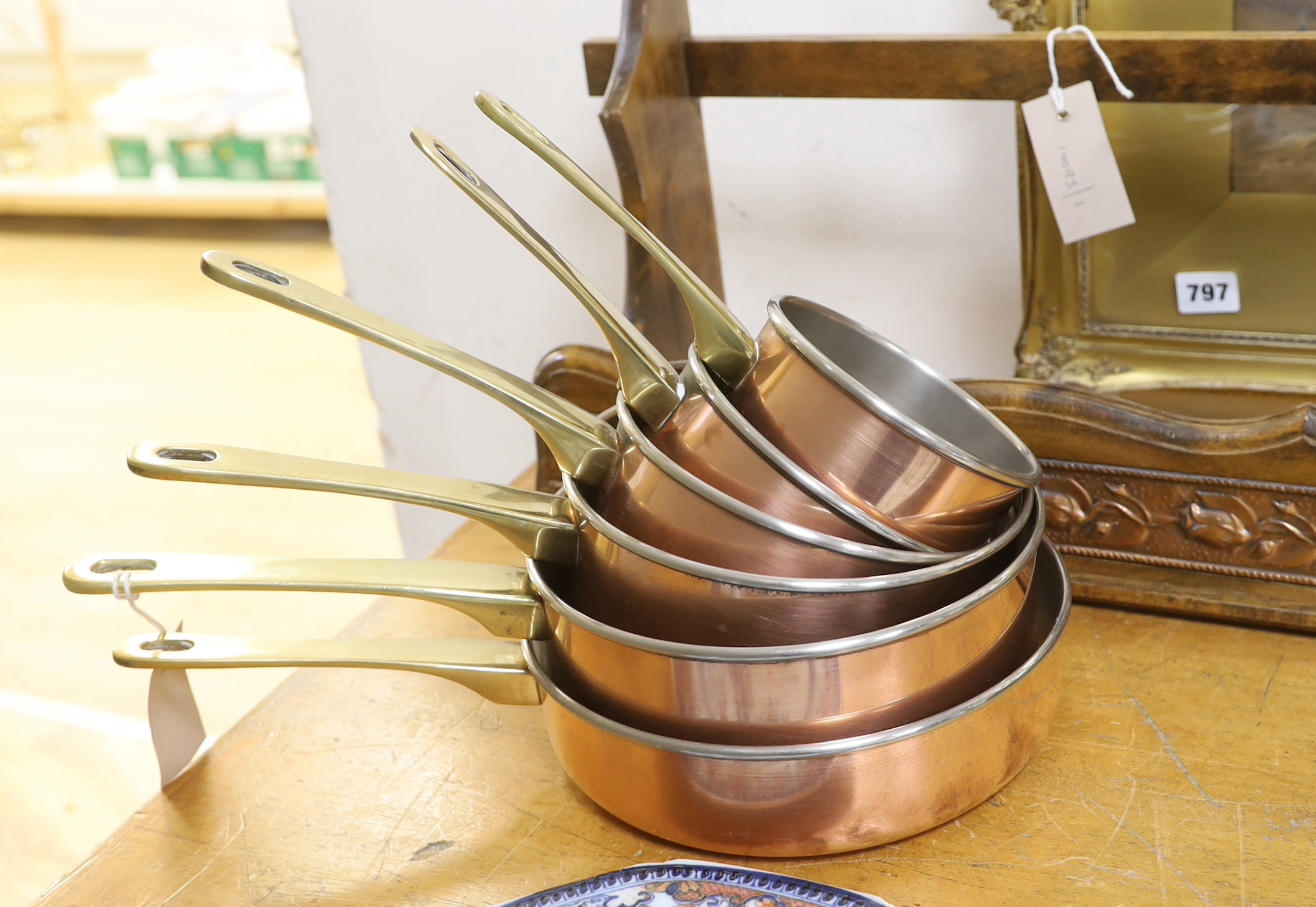 A graduated set of six copper and brass saucepans with beech hanging rack, 104cm wide